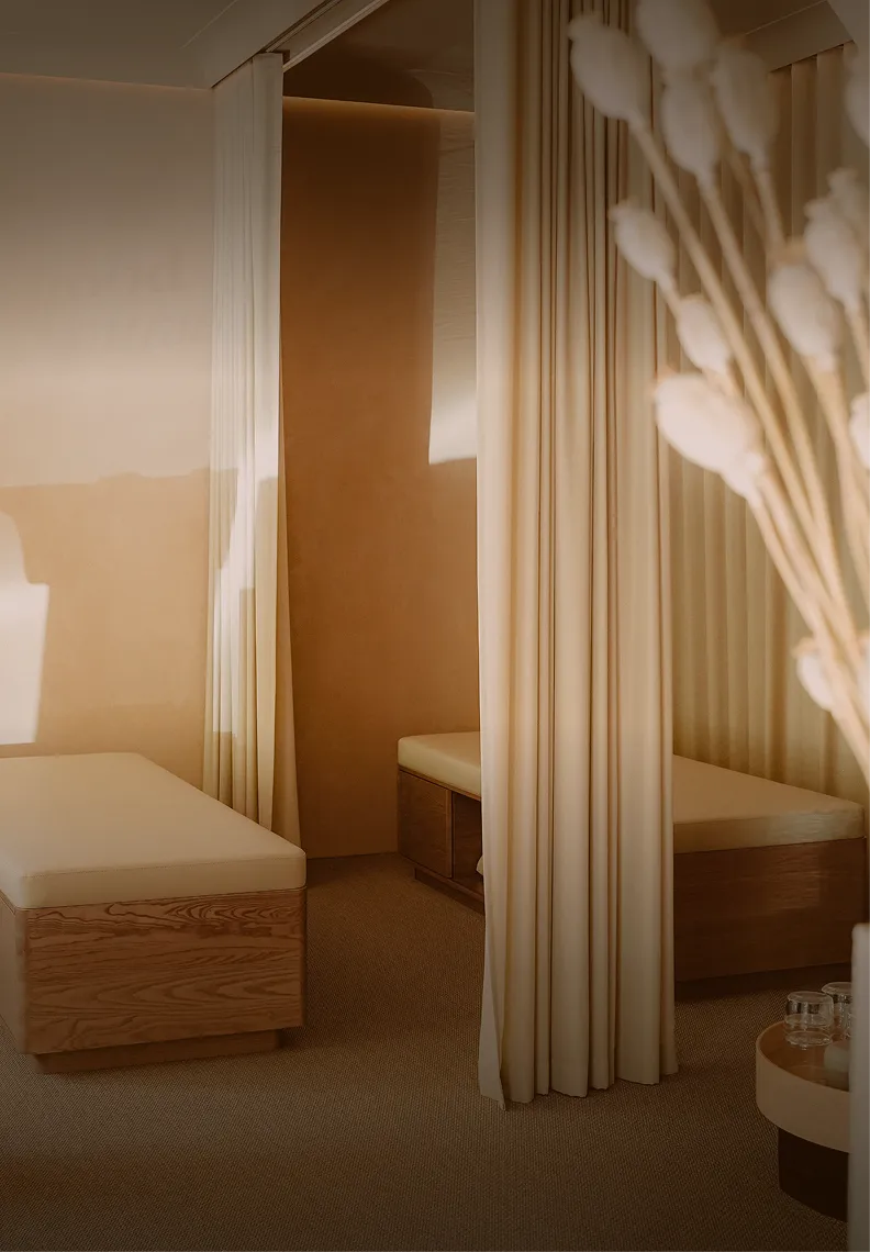 Acogedor Pluma Studio con dos bancos de madera, cojines beige y cortinas como separadores de ambientes bajo una luz cálida.