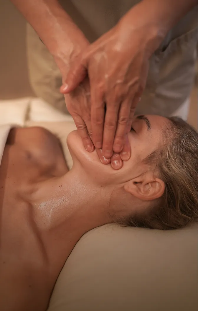 Una mujer se relaja durante un masaje facial y de cuello con manos con aceite.