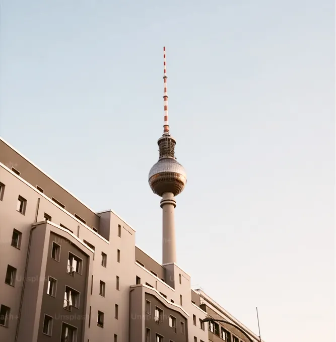 La torre de televisión de Berlín se alza hacia el cielo despejado detrás de un edificio residencial con muchas ventanas.
