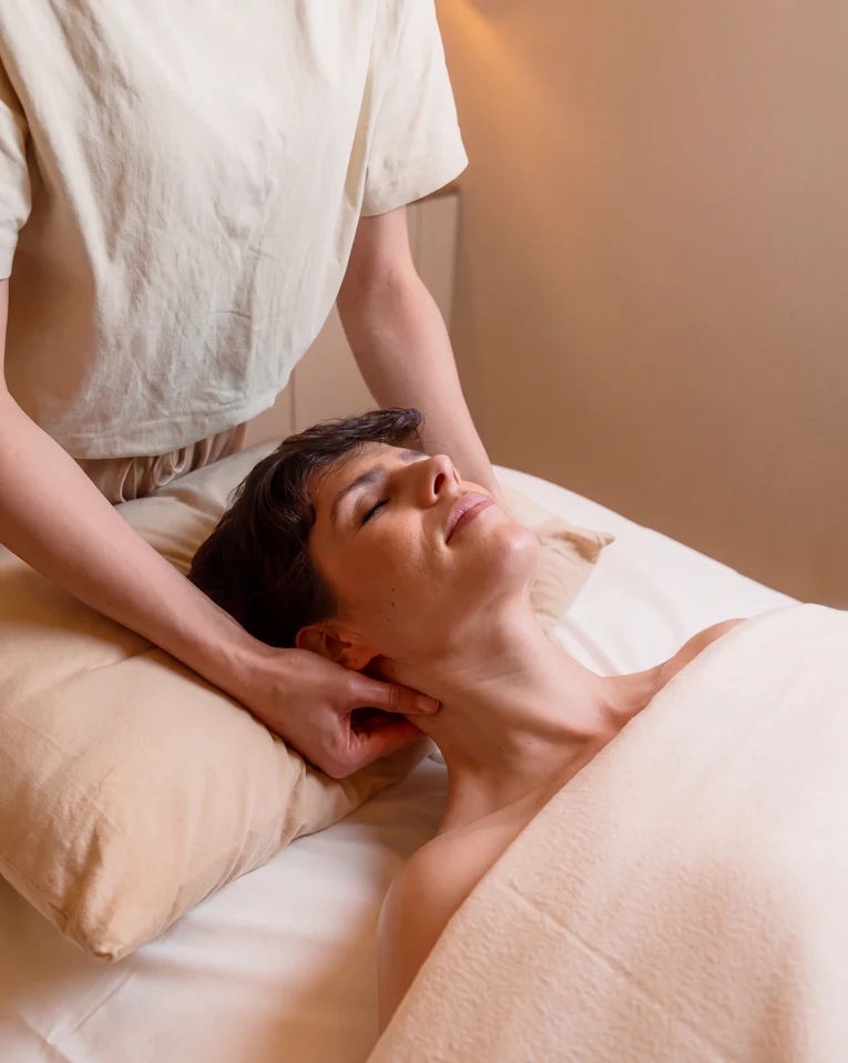 Una mujer se relaja con los ojos cerrados mientras recibe un suave masaje wellness en una camilla.