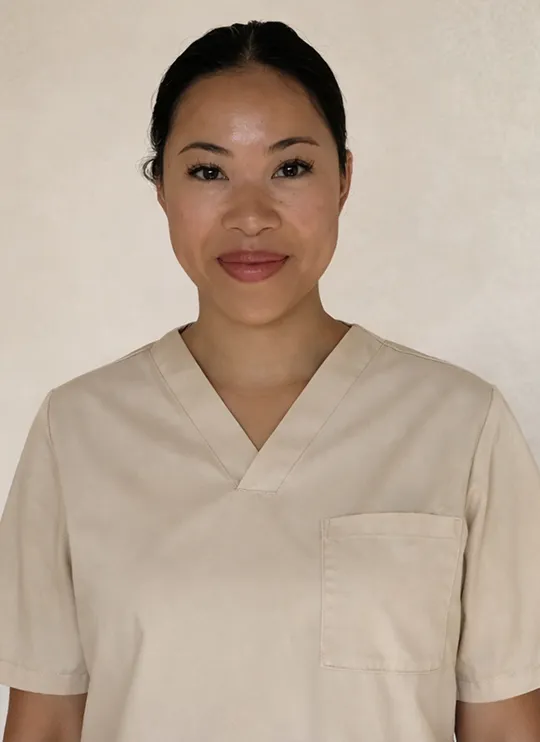 Expert de masaje de Pluma con el pelo recogido, vestida con uniforme sanitario beige y sonriendo amablemente.