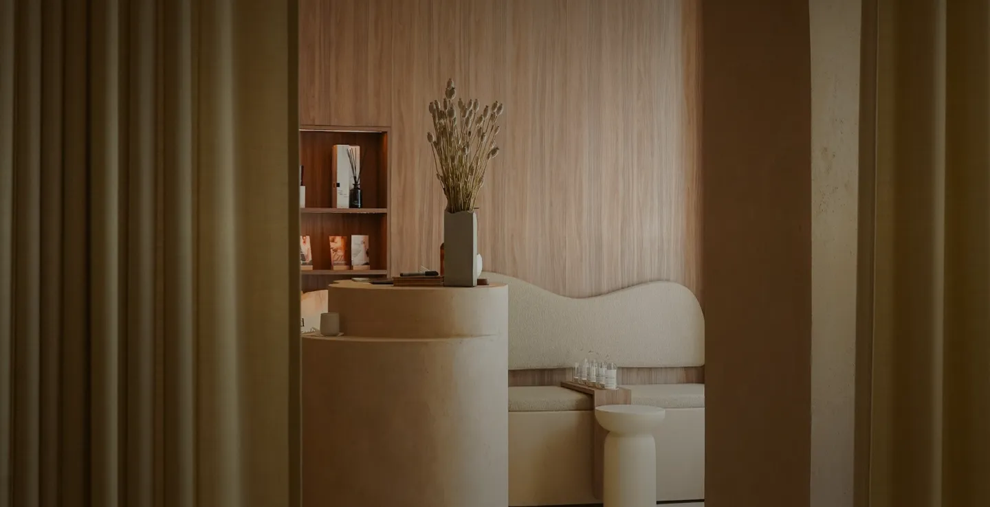 Sala de espera moderna con sofá beige, mesa redonda y flores secas en un jarrón.