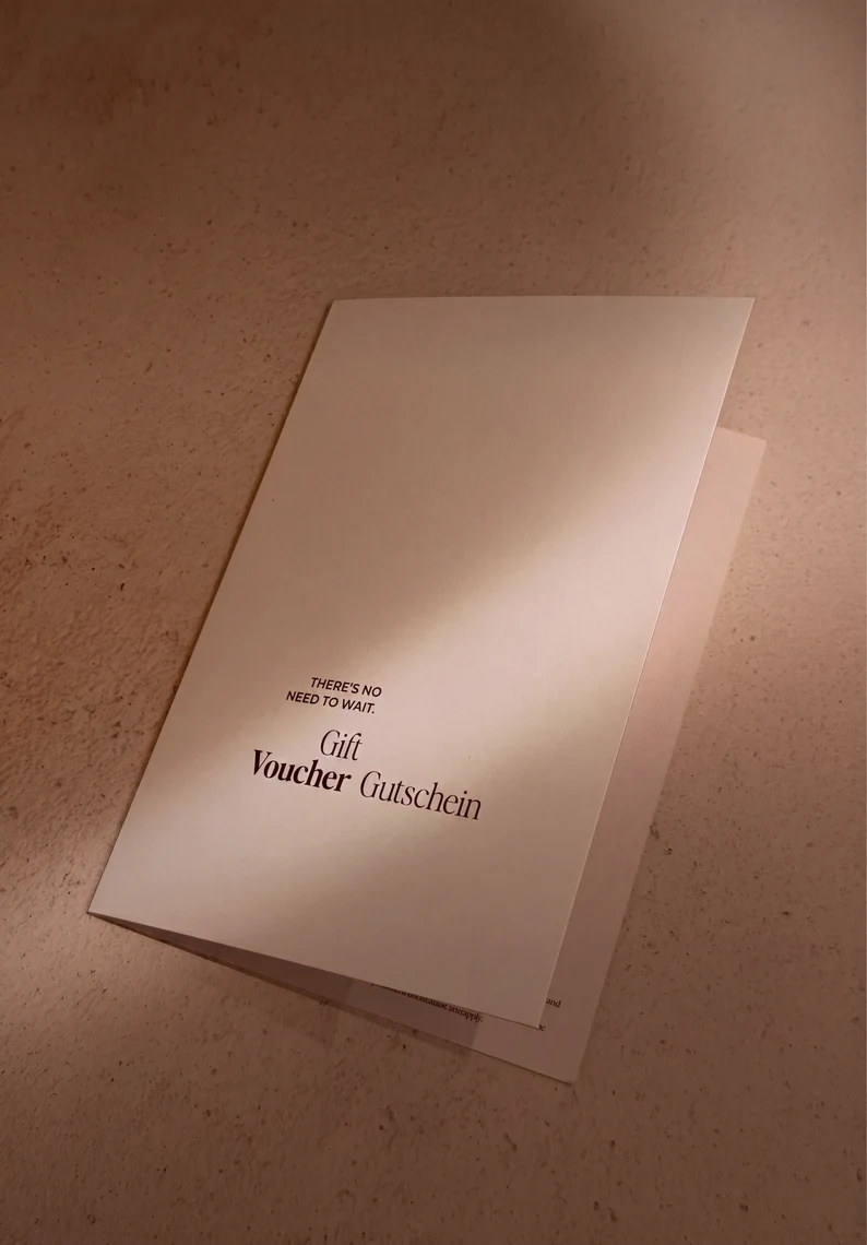 Una tarjeta regalo minimalista de la marca Pluma sobre fondo beige con el texto 'No hay motivo para esperar. Tarjeta regalo. Sé bueno contigo mismo.'