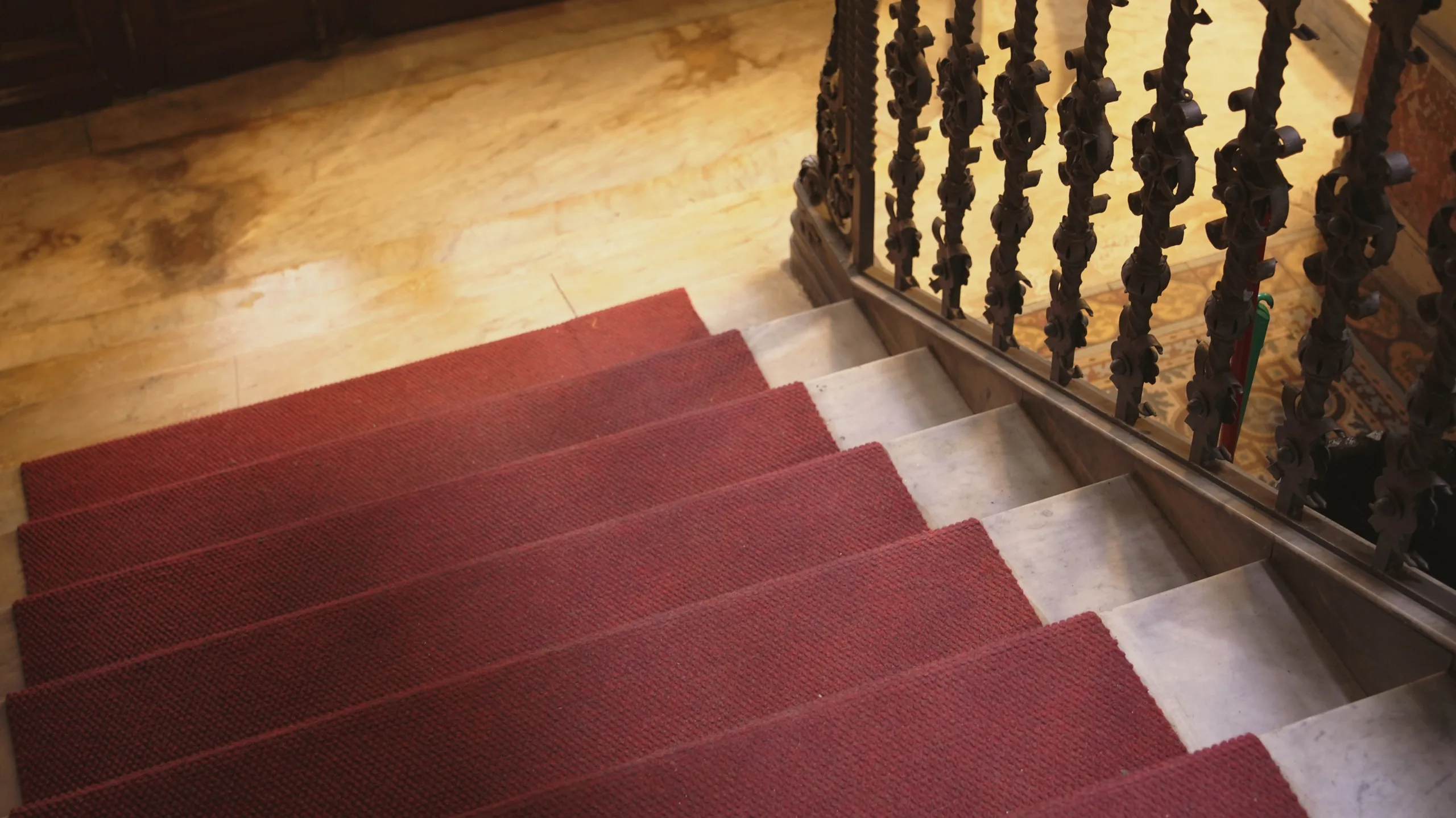 Escalera de la casa Pluma con alfombra roja y baranda de hierro forjado.